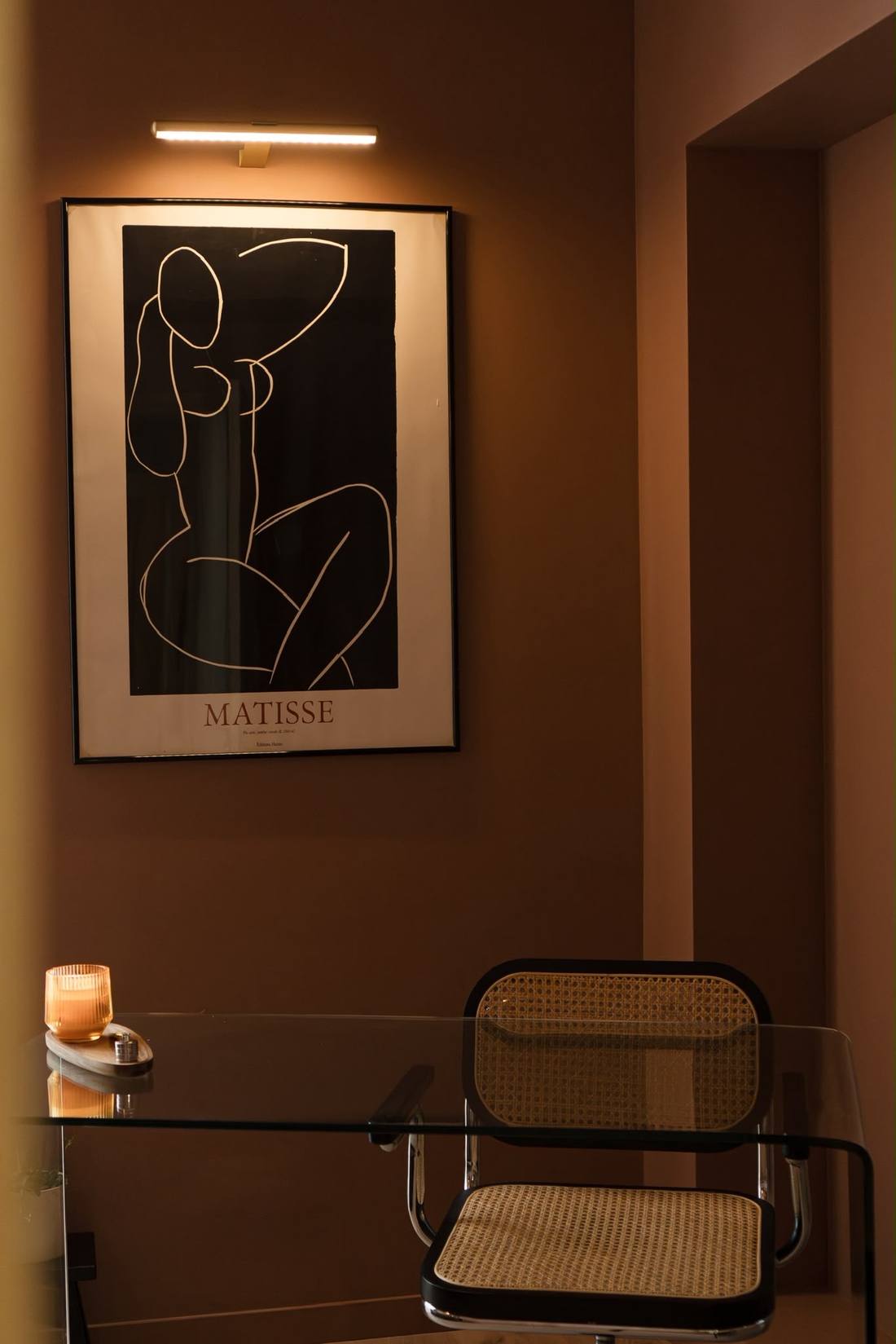 Bureau en verre avec chaise cannée sous une affiche Matisse